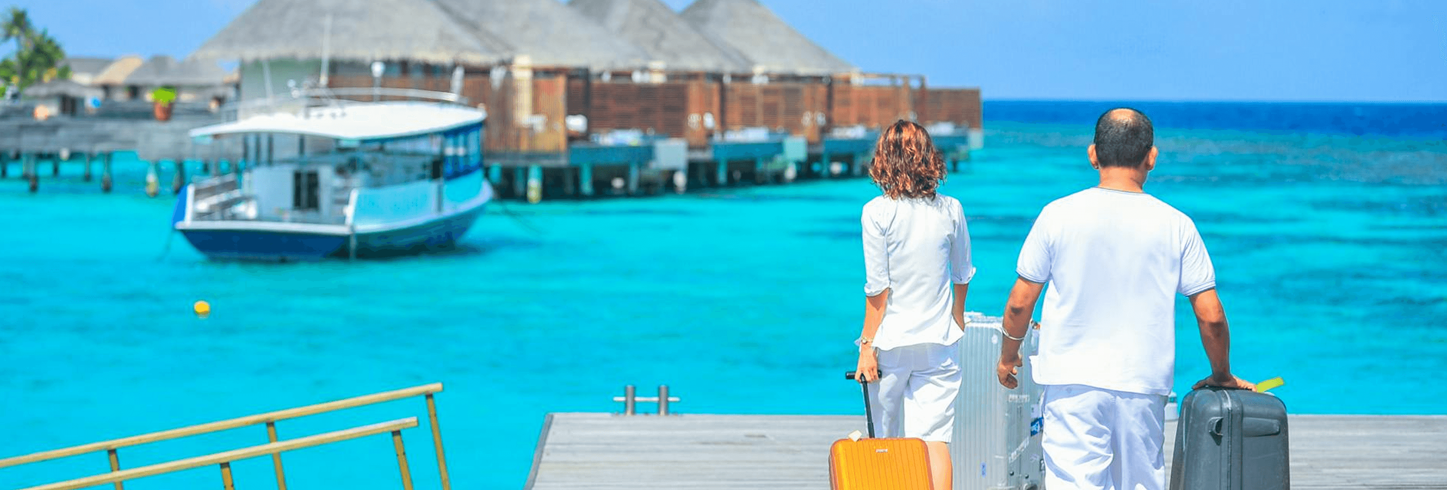 Couple with luggage walking on a tropical boardwalk over turquoise water